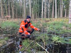 Mann hockt auf nasser Fläche im Wald